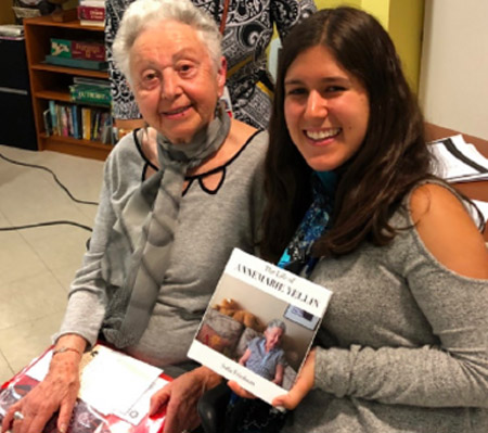 An alumni sits next to a Holocaust survivor and is holding a book she wrote about her.