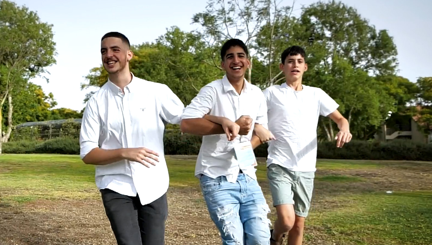 Three teens skipping in a field with their arms locked around another.